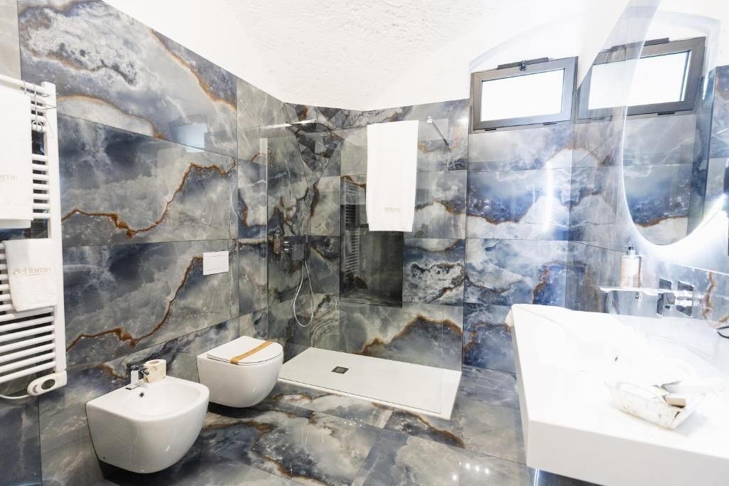 Een moderne badkamer met een marmeren wand, een badkuip, een hygiëneschuiver en een douche.