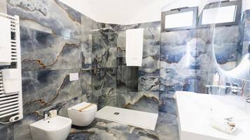 Een moderne badkamer met een marmeren wand, een badkuip, een hygiëneschuiver en een douche.