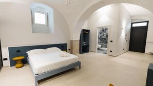 A bedroom with a bed, a small table, a wardrobe, and a bathroom with a marble wall. - BeHome al Porto (Trani)