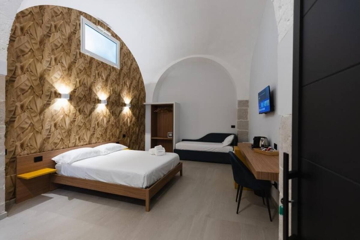 Una habitación de hotel moderna con cabecera de madera, cama, escritorio y televisor.