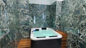 A modern bathroom with a marble wall, a wooden bench, and a hot tub. - BeHome al Porto (Trani)