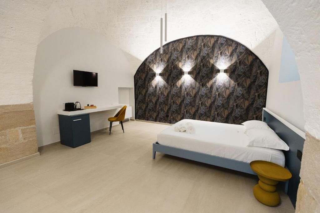 A bedroom with a bed, a desk, a chair, a TV, and a unique curved wall design.