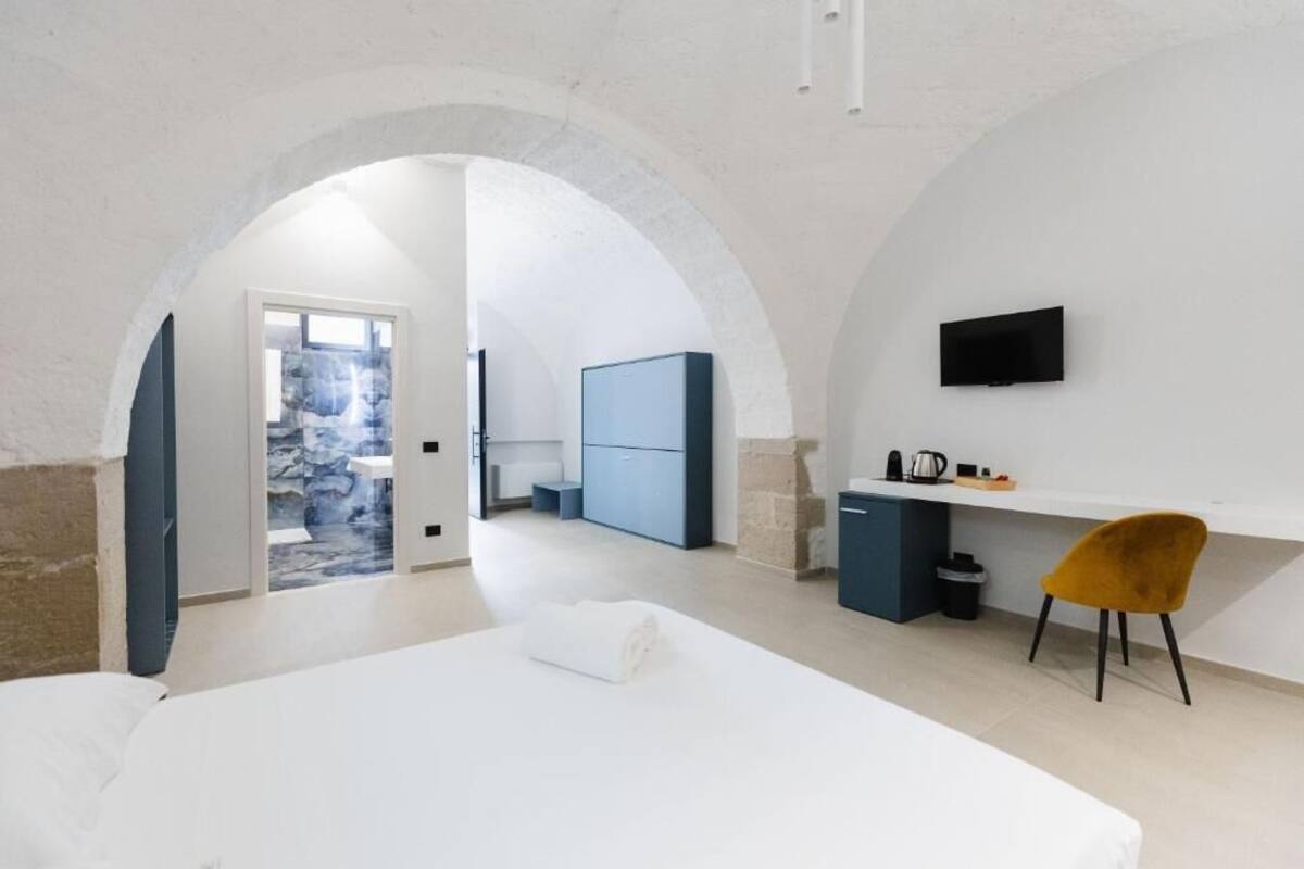 Una habitación moderna con cama, escritorio, silla, televisor y vistas a un espacio exterior.