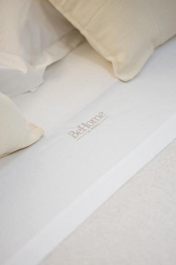 A bed with a white sheet and a pillow with the text 'Bellehome' on it.