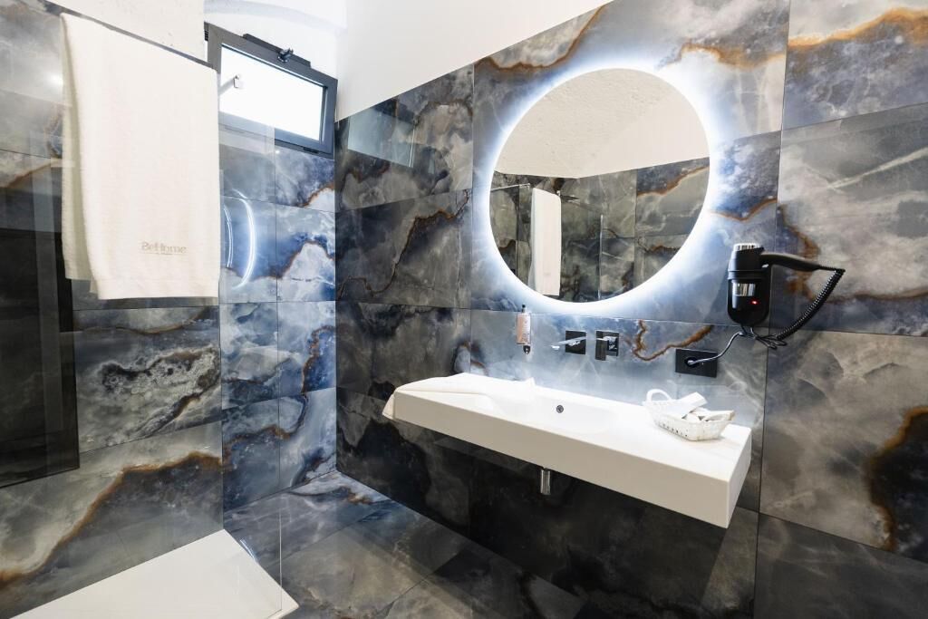 A bathroom with a marble wall, a sink, a mirror, and a towel rack.
