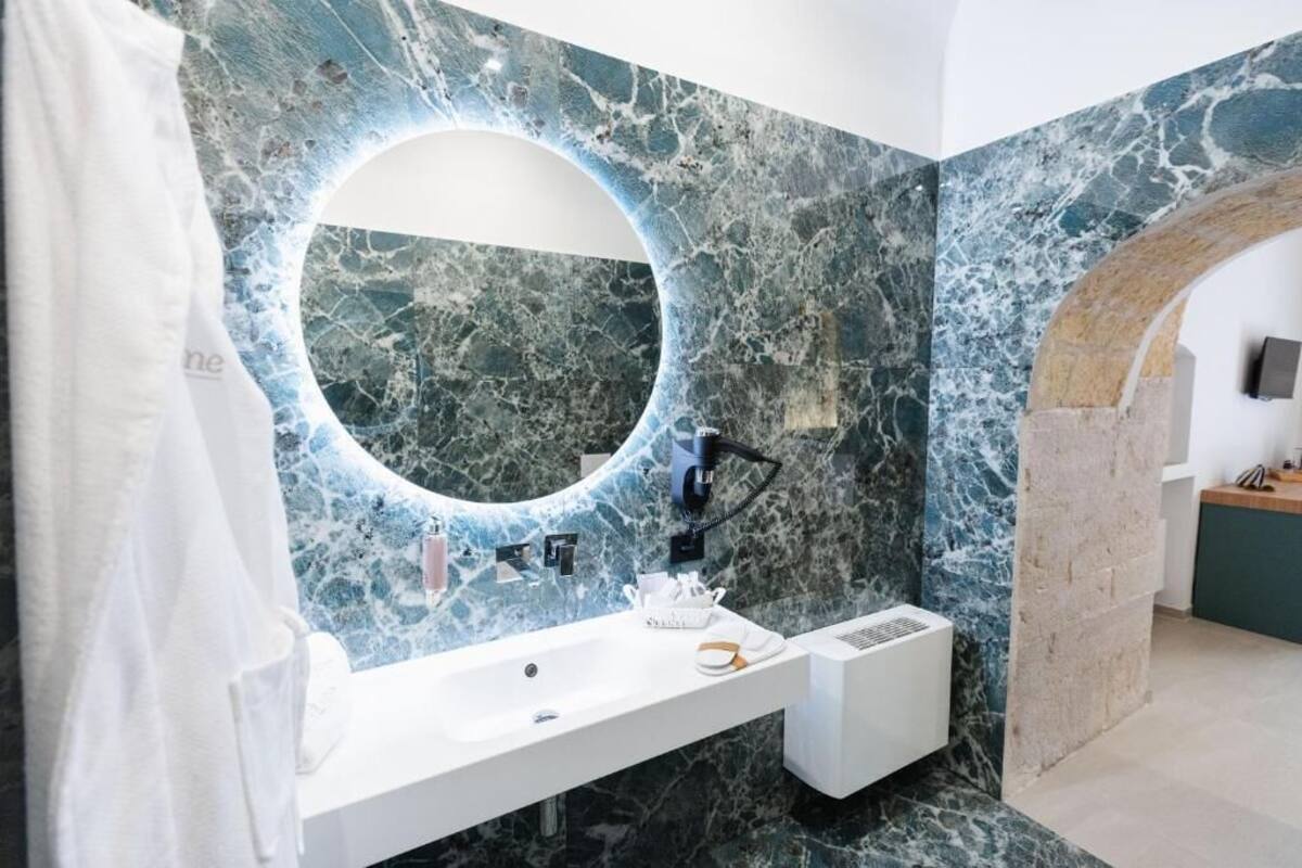 Un baño con un lavamanos de mármol, un espejo grande y un arco de piedra.