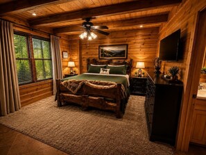 Ein schlicht eingerichtetes Schlafzimmer im Chalet-Stil mit einem Bett, einem Deckenventilator, einem Fernseher und einem Fenster mit Vorhängen.
