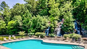 Ein rechteckiger Swimmingpool mit Wasserfall, umgeben von Liegestühlen und einer gepflasterten Terrasse.