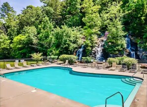 Ein rechteckiger Swimmingpool mit Wasserfall, umgeben von Liegestühlen und einer gepflasterten Terrasse.