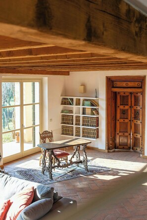 Une pièce avec un plafond en bois, une table entourée de chaises, une bibliothèque et une grande porte en bois.