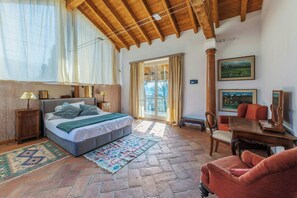 Une chambre à coucher avec un lit, un plafond en bois, une fenêtre avec des rideaux, une porte donnant sur l’extérieur, une petite table et une chaise.