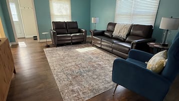 Un salon avec un mur bleu, deux canapés en cuir, un fauteuil bleu, un plancher en bois, un ventilateur de plafond et une porte.