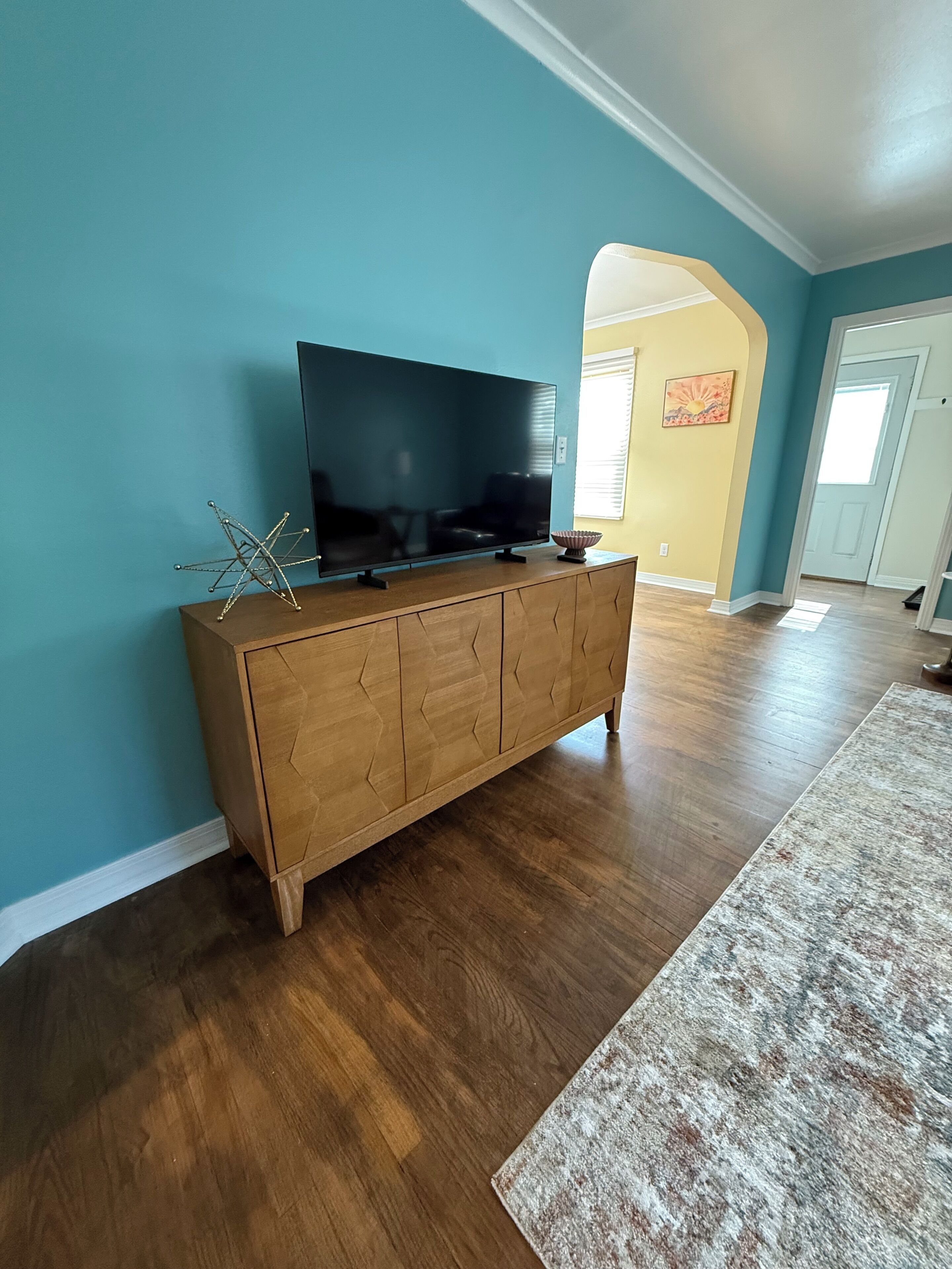 Un salon avec un meuble en bois, un téléviseur à écran plat et un tapis à motifs.