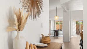 A modern interior with a wooden table, a white vase with pampas grass, a woven basket, and a hanging light fixture. - Sandpiper by Nest Villas | 5BR Estate | Large Pool (Indio)