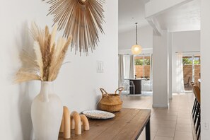 A modern interior with a wooden table, a white vase with pampas grass, a woven basket, and a hanging light fixture. - Sandpiper by Nest Villas | 5BR Estate | Large Pool (Indio)