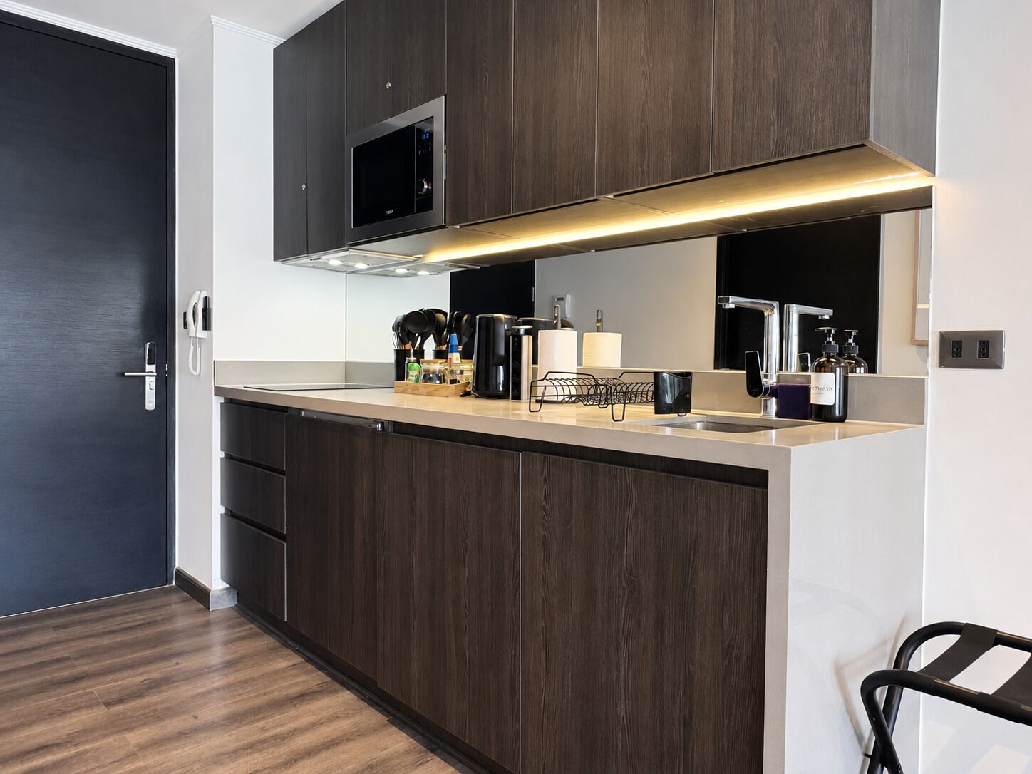 Una cocina moderna con armarios de madera oscura, un microondas de acero inoxidable, un horno empotrado y un espejo grande sobre la encimera.