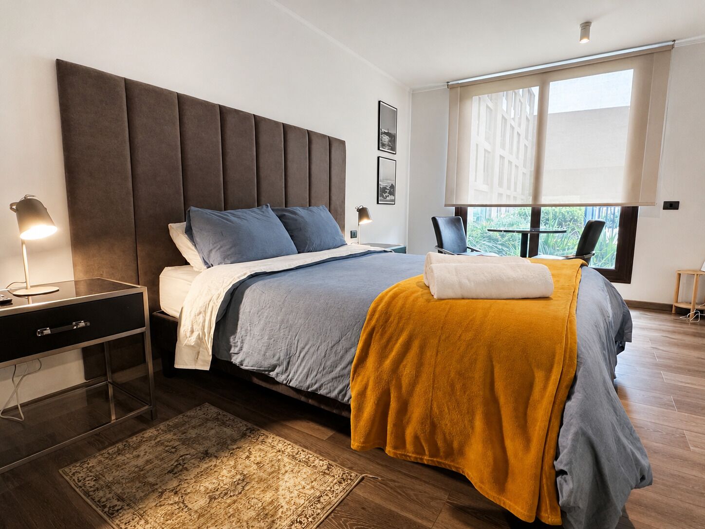 A modern bedroom with a large bed, bedside tables, a desk, and a window with a view.