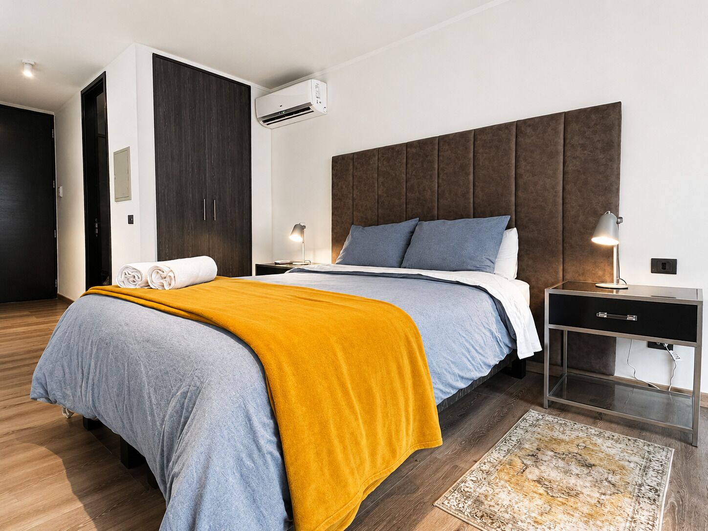 Een moderne hotelkamer met een groot bed, een nachtkastje, een bureau en een airconditioning.