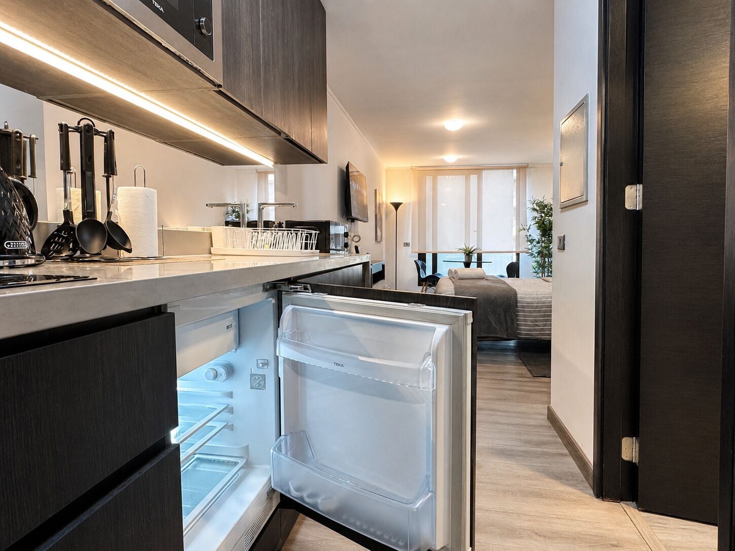 Een moderne keuken met een inbouwkoelkast, een eethoek met een tafel en stoelen, en een slaapkamer met een bed en raam.