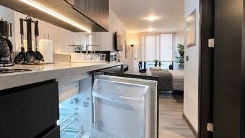 Een moderne keuken met een inbouwkoelkast, een eethoek met een tafel en stoelen, en een slaapkamer met een bed en raam.