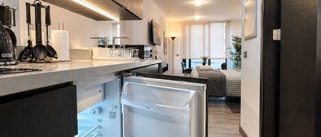 Una cocina moderna con refrigerador empotrado, un comedor con mesa y sillas, y un dormitorio con cama y ventana.