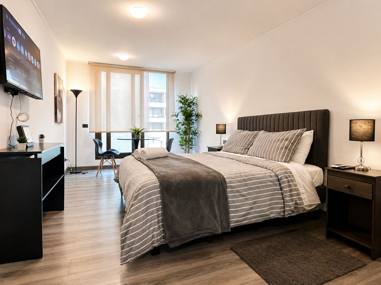 A modern bedroom with a bed, bedside tables, a desk, a chair, a TV, and a window.