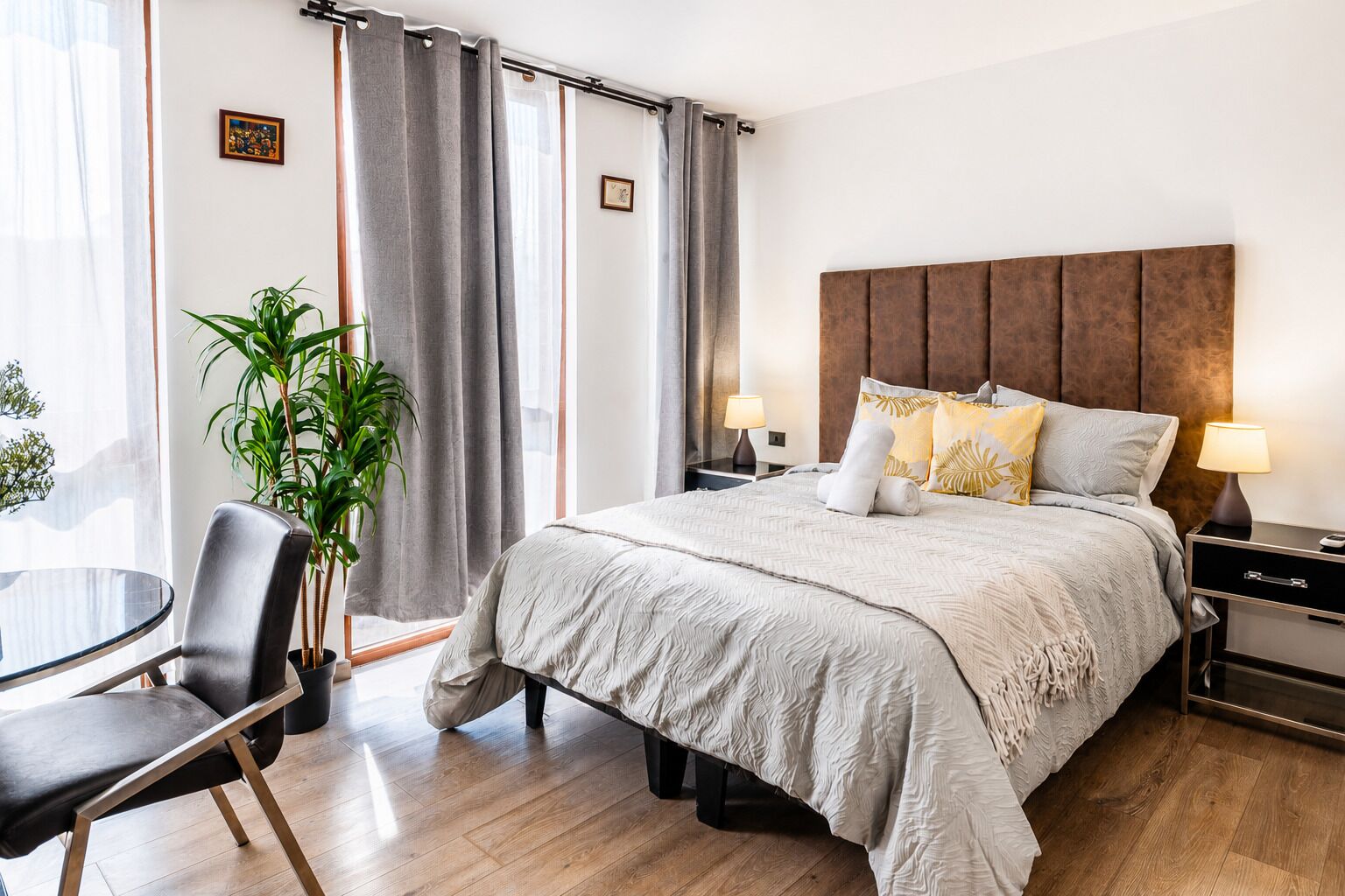 Habitación de hotel moderna con una cama grande, un escritorio con silla, una planta en maceta y vistas a la ciudad.