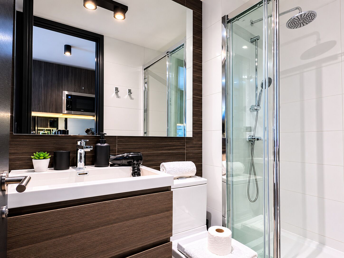 A modern bathroom with a glass shower enclosure, a white sink with a dark wood vanity, and a large mirror above the vanity.