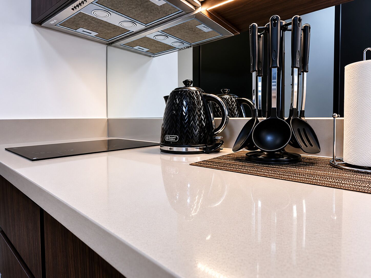 A modern kitchen with a sleek countertop, a kettle, a coffee maker, and a set of black kitchen utensils.