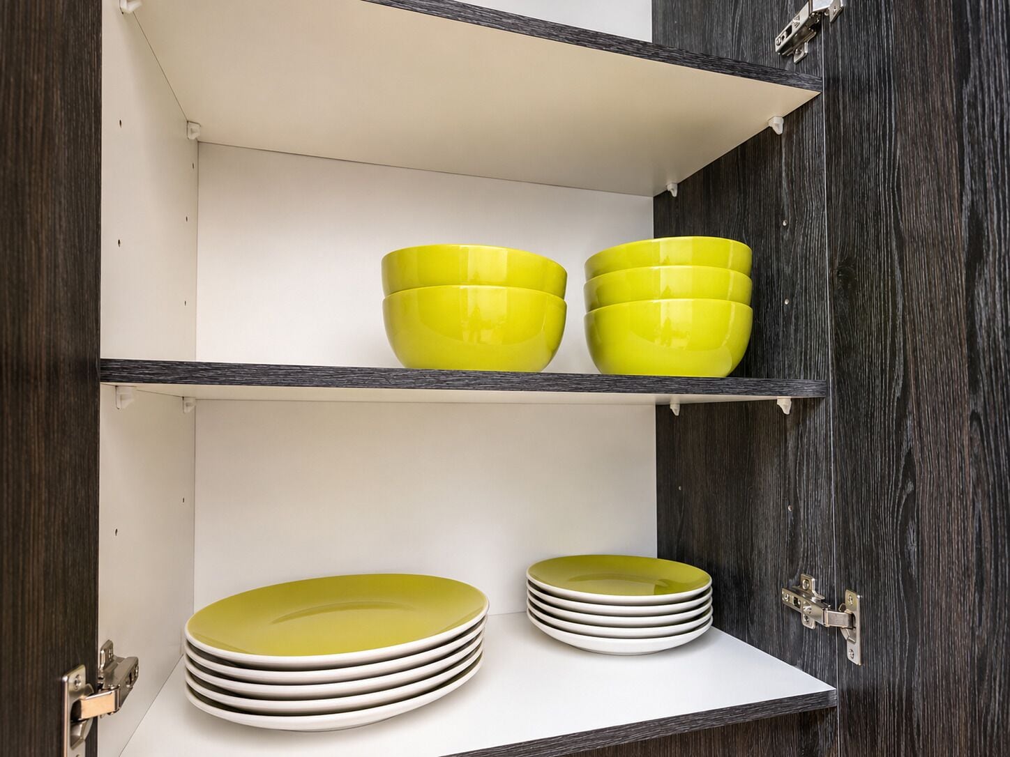 A kitchen with white cabinets, a wooden door, and a shelf with yellow bowls and stacked plates.