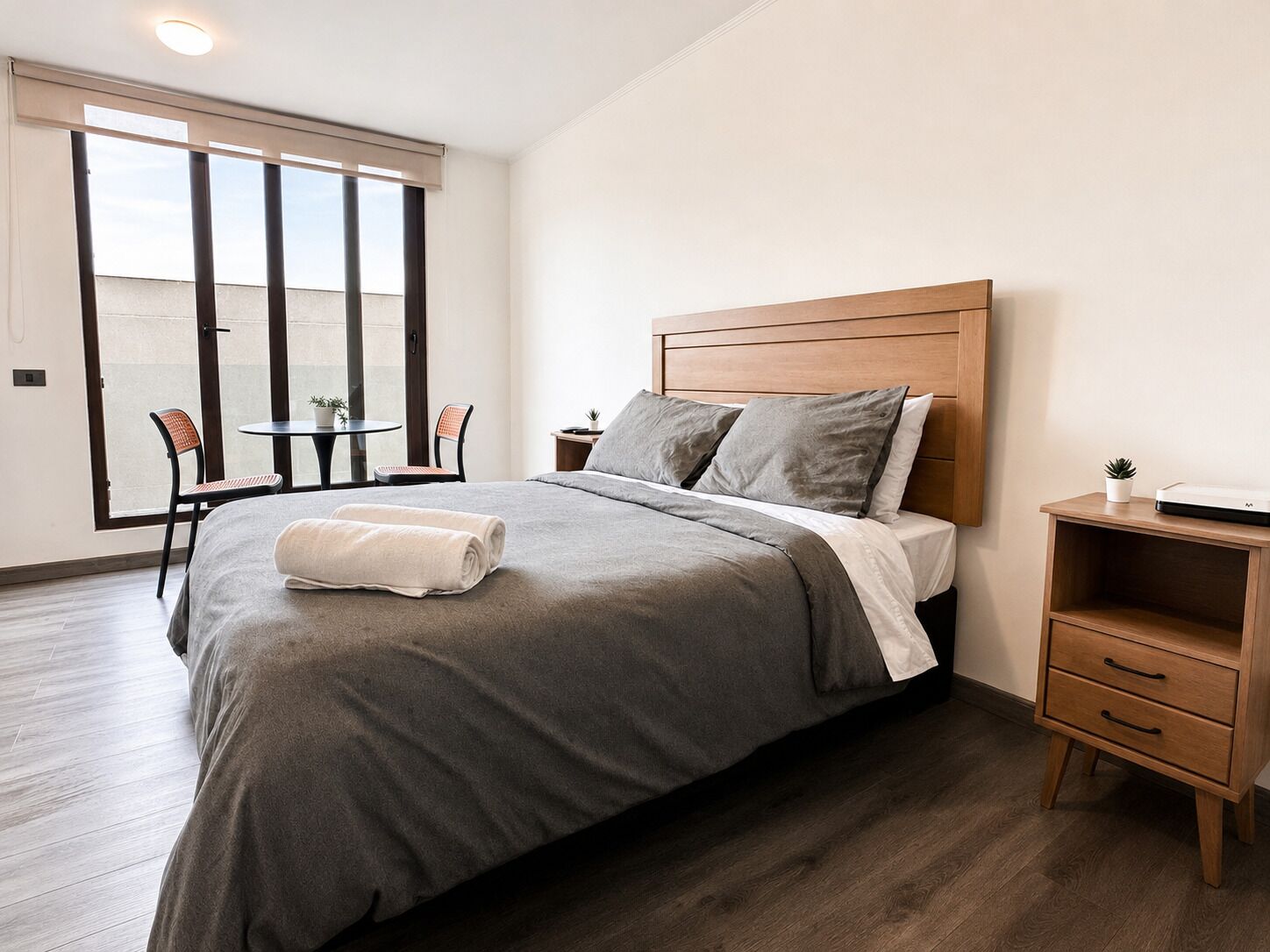 Une chambre à coucher avec un lit, des tables de chevet, une petite table avec des chaises et une vue par la fenêtre.