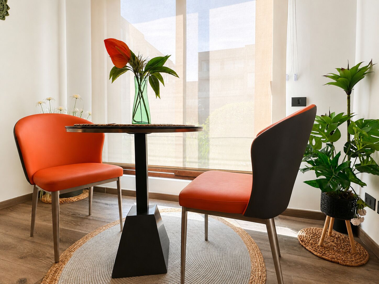 A modern room with two orange chairs, a black table, and a green vase with plants.