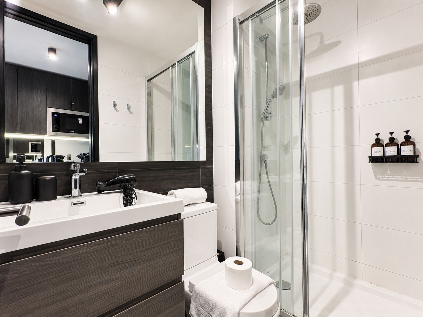 A modern bathroom with a glass-enclosed shower, a white sink with a dark countertop, and a large mirror above the sink.