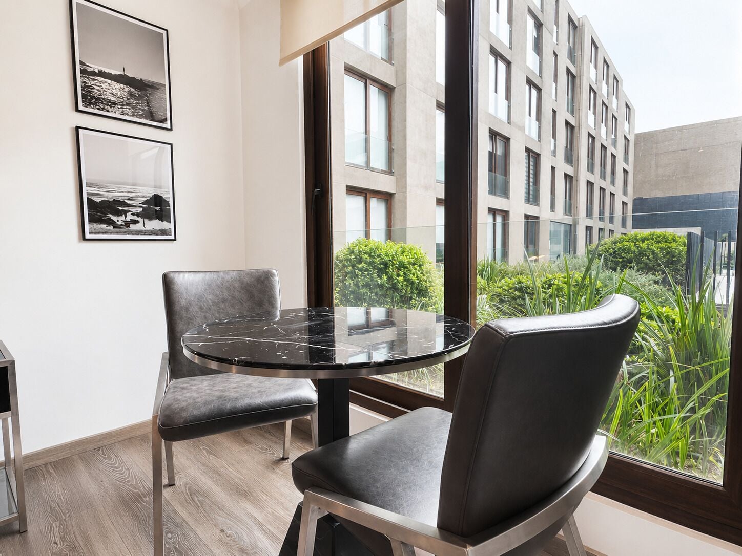 A modern room with a round table, two chairs, and a large window offering a view of a building and greenery.