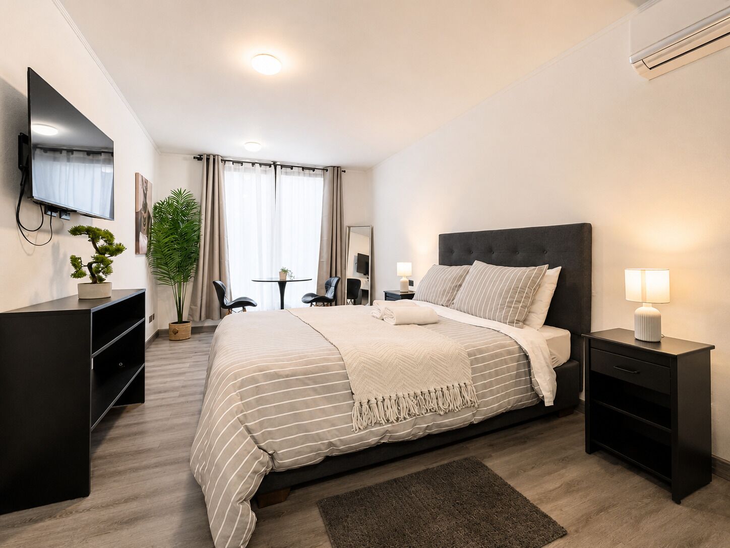 A modern hotel room with a large bed, bedside tables, a TV, and a desk with a chair.