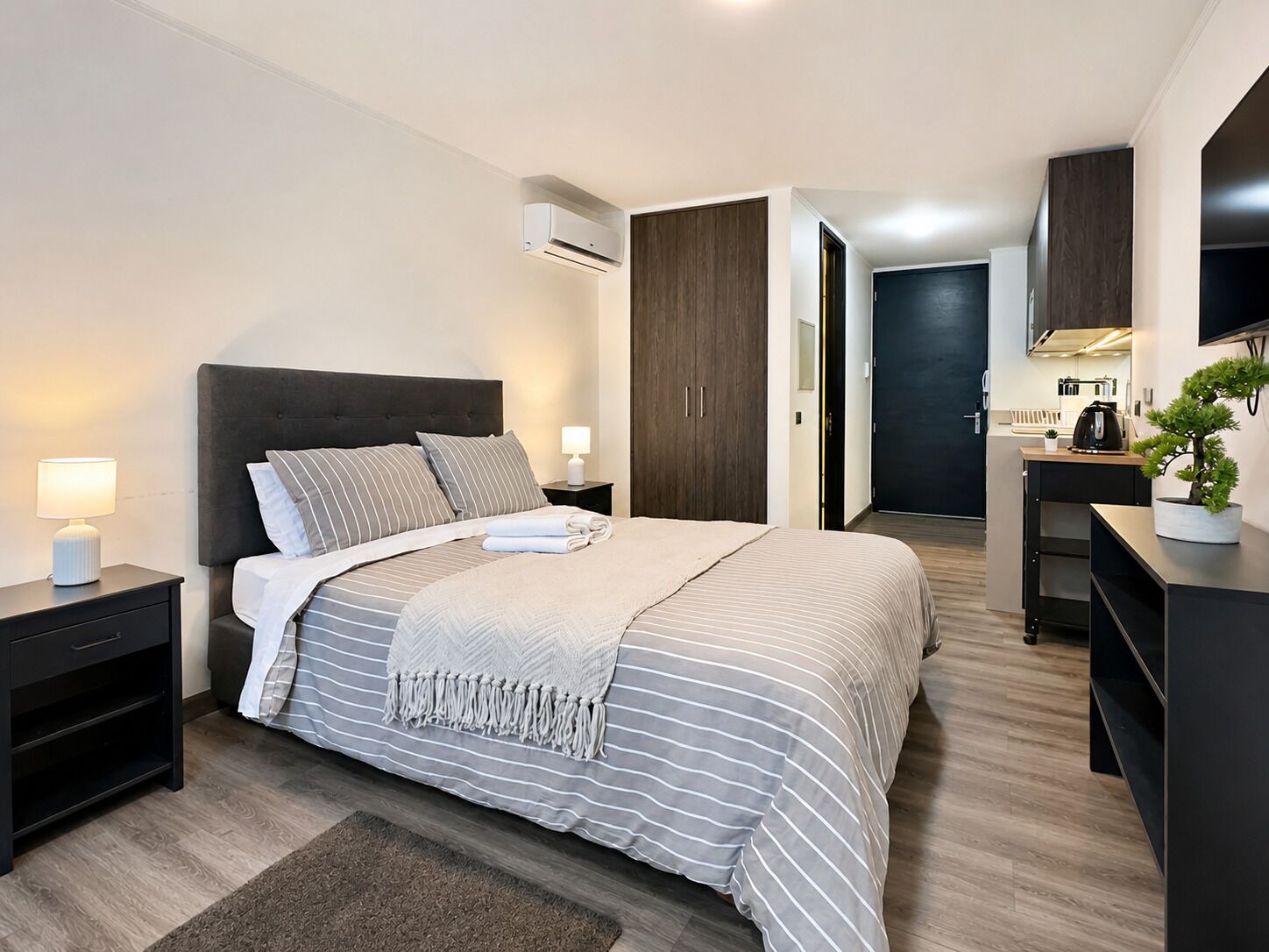 Een moderne slaapkamer met een bed, nachtkastjes, een bureau, een stoel, een airconditioner en een televisie.
