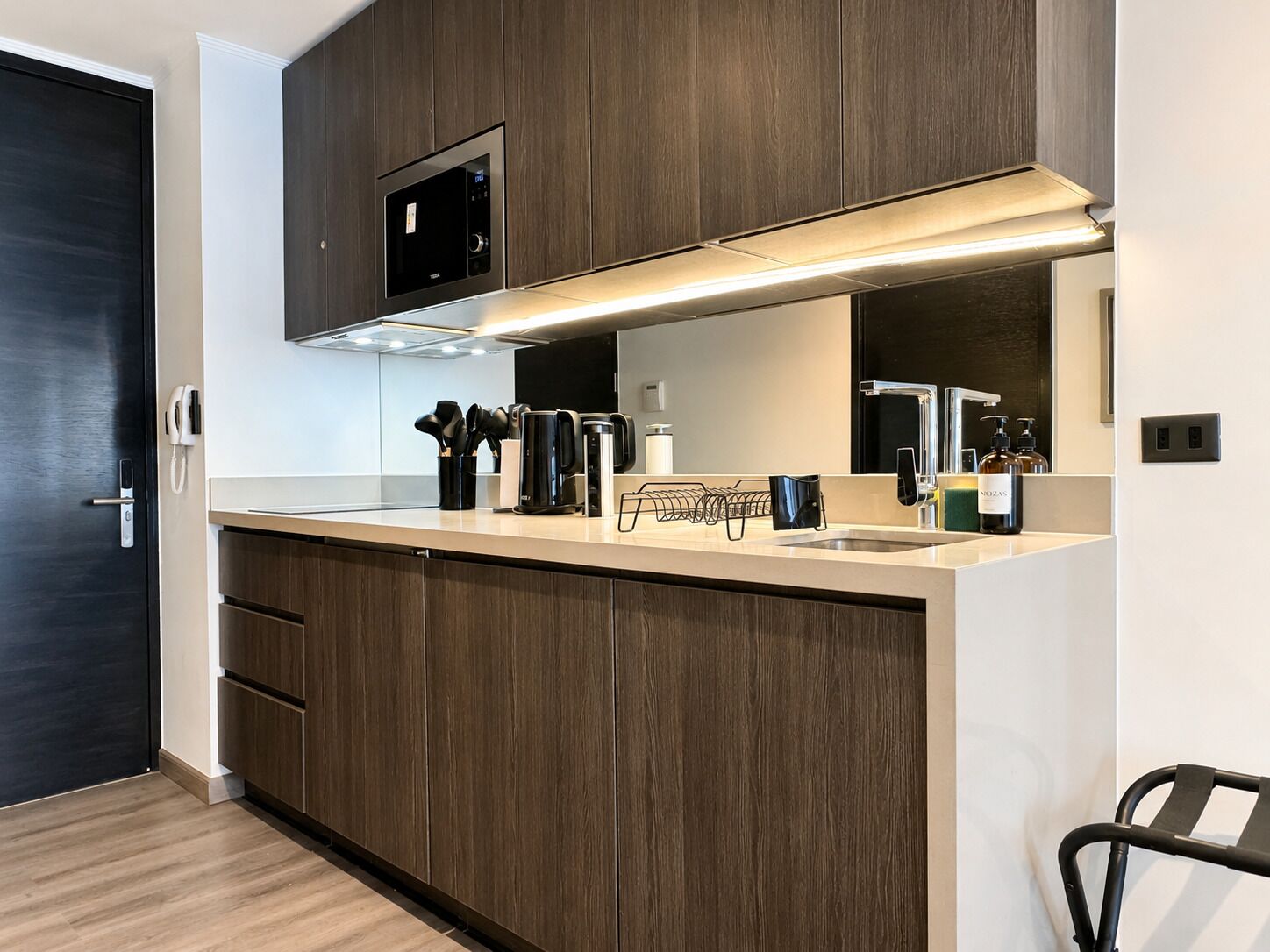 A modern kitchen with dark wood cabinets, a built-in microwave, and a stainless steel sink.