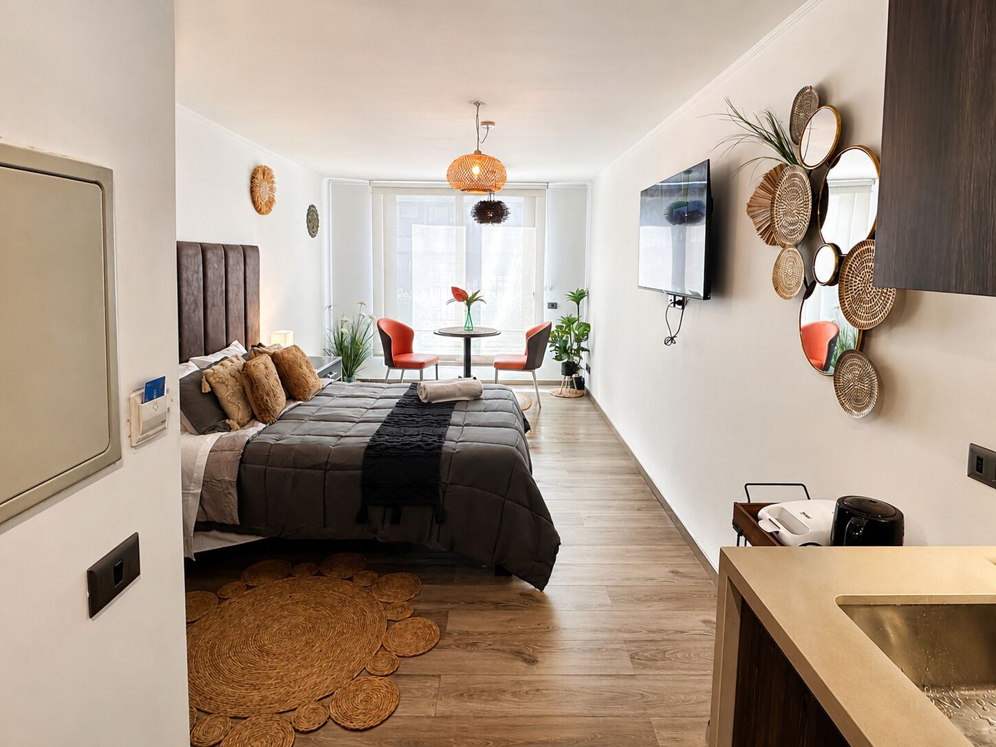 Una habitación de hotel moderna con una cama, una pequeña mesa, sillas, un televisor y un espejo montado en la pared.