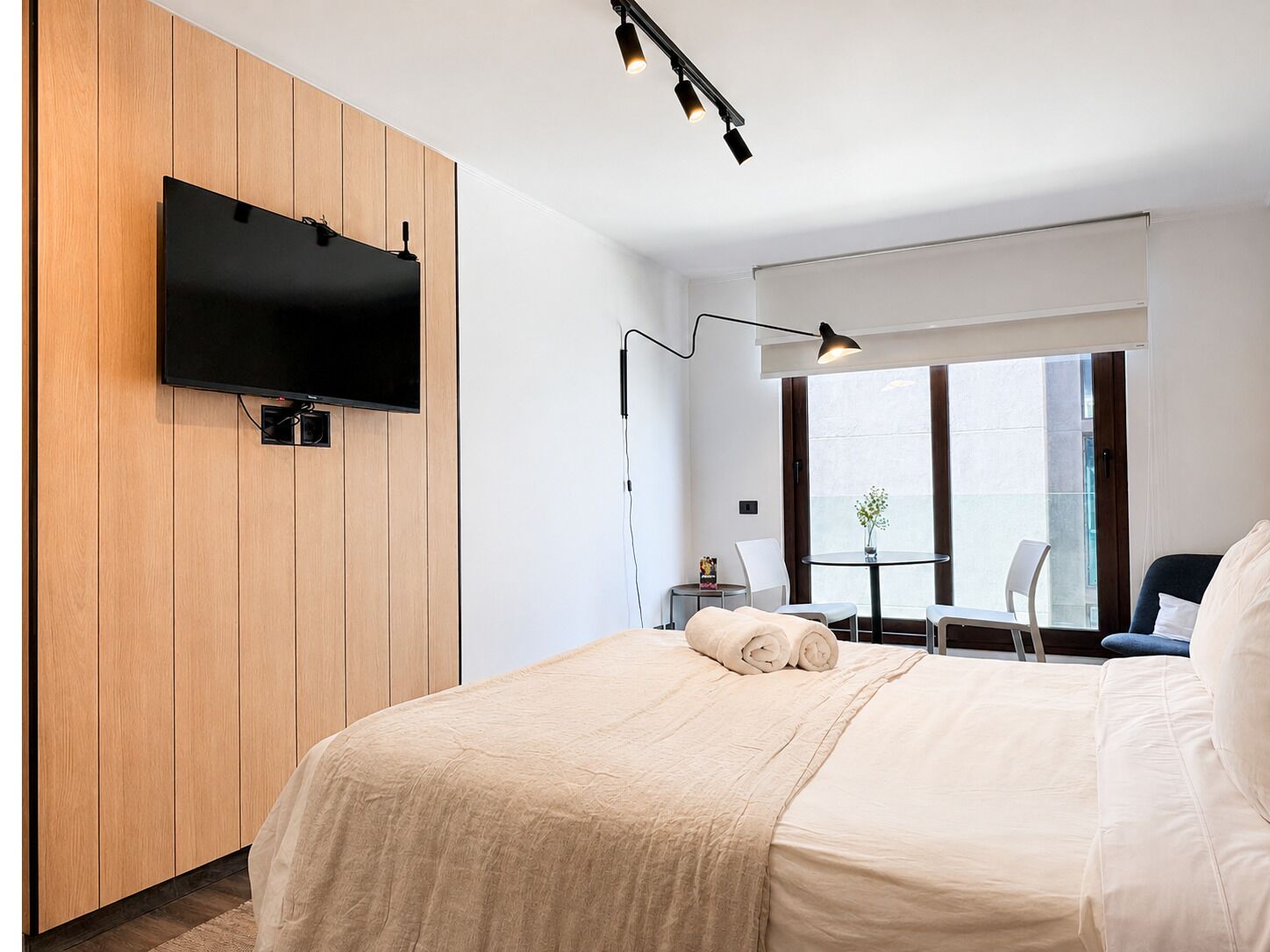 Habitación de hotel moderna con una cama grande, un televisor de pantalla plana montado en una pared de paneles de madera, un escritorio con una silla y una ventana con vistas.
