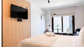 Een moderne hotelkamer met een groot bed, een flatscreen televisie bevestigd aan een houten wandpaneel, een bureau met stoel en een raam met uitzicht.