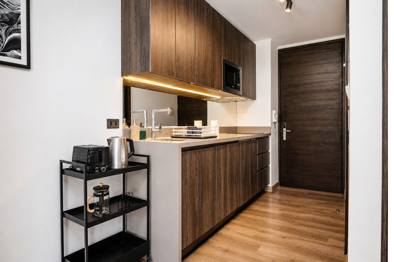 A modern kitchen with wooden cabinets, a built-in microwave, and a coffee machine on a black shelf.
