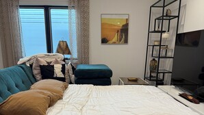Une chambre à coucher avec un lit, un canapé, une télévision, une étagère et une fenêtre avec des rideaux.