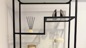 Une étagère métallique noire contenant divers objets, notamment un vase, une lampe et des objets décoratifs.