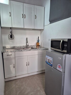 A kitchen with white cabinets, a stainless steel sink, a microwave, and a refrigerator. - Burwood Breeze Retreat AC + WiFi + Hot water (Retreat Heights)