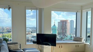 Una sala de estar moderna con un sofá, una mesa redonda de centro y un televisor de pantalla plana. Amplias ventanas ofrecen vistas a la ciudad.
