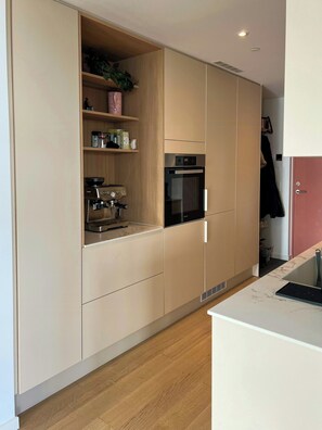 Una cocina moderna con electrodomésticos integrados, estantes de madera y encimera de mármol.