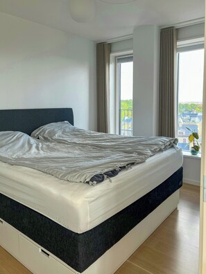 A modern bedroom with a large bed, a headboard, and a window with curtains. - Panoramic view over Carlsberg Quarter (København)