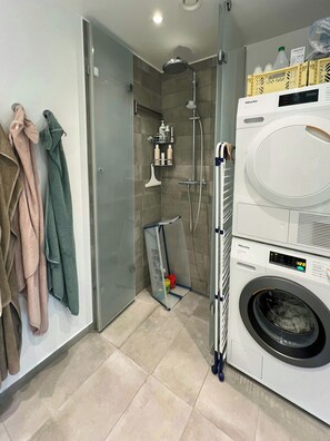 A modern bathroom with a glass shower enclosure, a built-in washing machine, and towels hanging on the wall. - Panoramic view over Carlsberg Quarter (København)