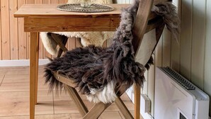 A wooden dining table with a woven placemat and a candle, a rustic chair with a fur throw, and a wall-mounted heater. - Wagon with view over Lake Ollerup (Vester Skerninge)