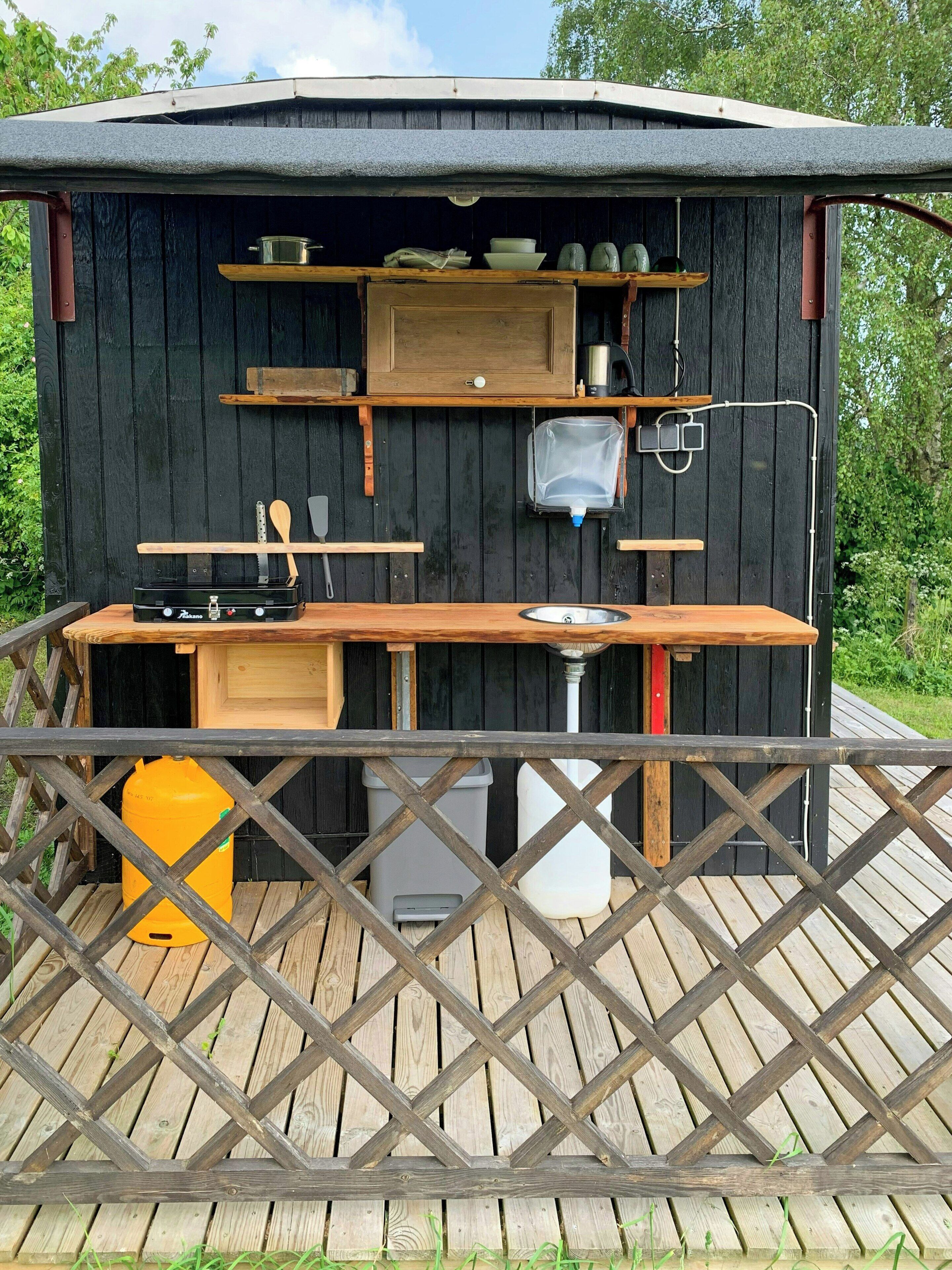 Een houten buitenkeuken met een barbecue, planken en een spoelbak.